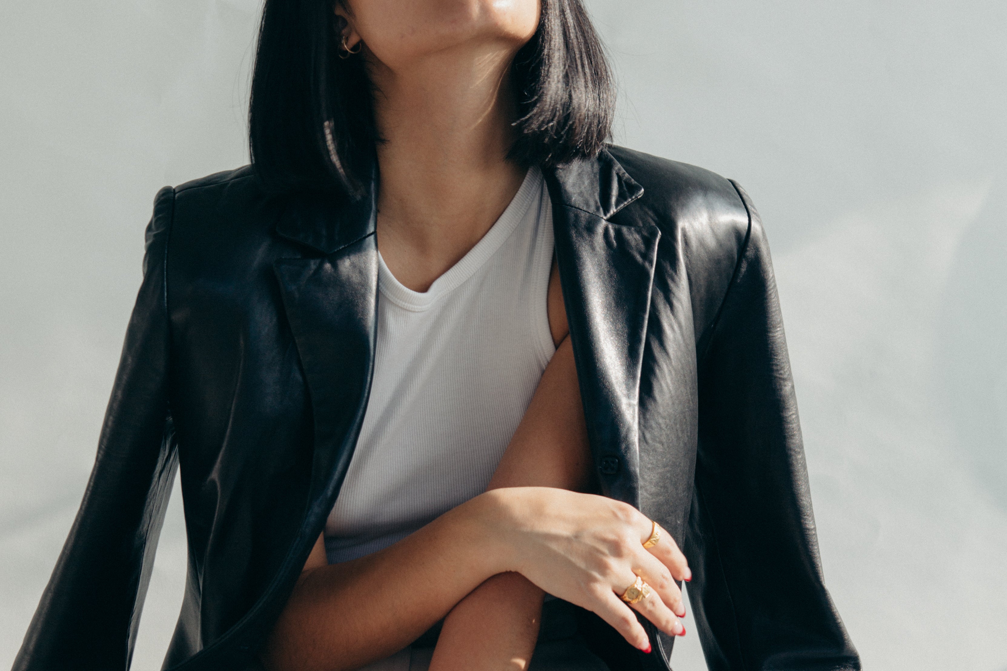 Frau in schwarzer Lederjacke über weißem Top, Nahaufnahme ihres Arms mit goldenen Ringen und dezentem Ohrschmuck, minimalistisches Styling im natürlichen Licht – Statement-Look für zeitlosen, modernen Schmuck von Fraeulein Matilda.
