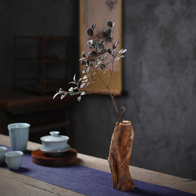 Das Bild zeigt eine rustikale Holzvase mit Eukalyptusblättern und Beeren auf einem Holztisch. Daneben befindet sich keramisches Teegeschirr in gedämpften Blautönen.