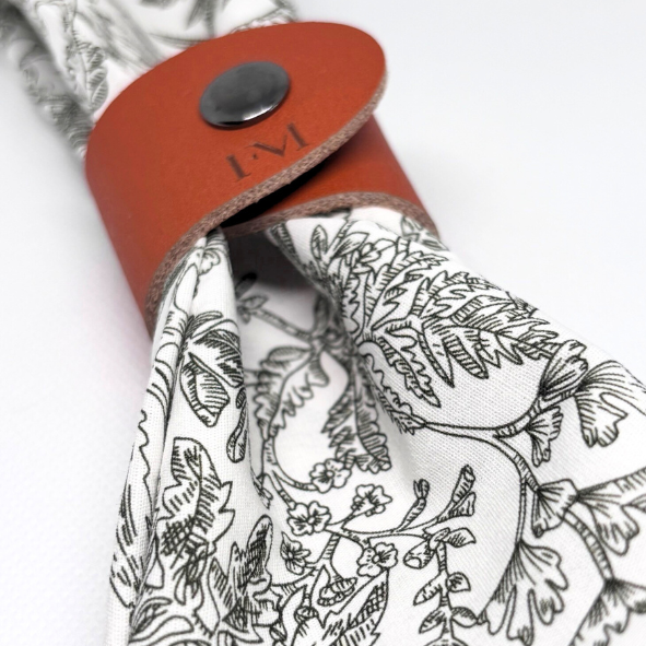 Naturweißes Baumwolltuch mit feinem botanischem Linienmuster, stilvoll gebunden mit einer cognacfarbenen Leder-Manschette mit FM-Prägung – elegantes Detail aus der Home | Living Kollektion von Fraeulein Matilda.