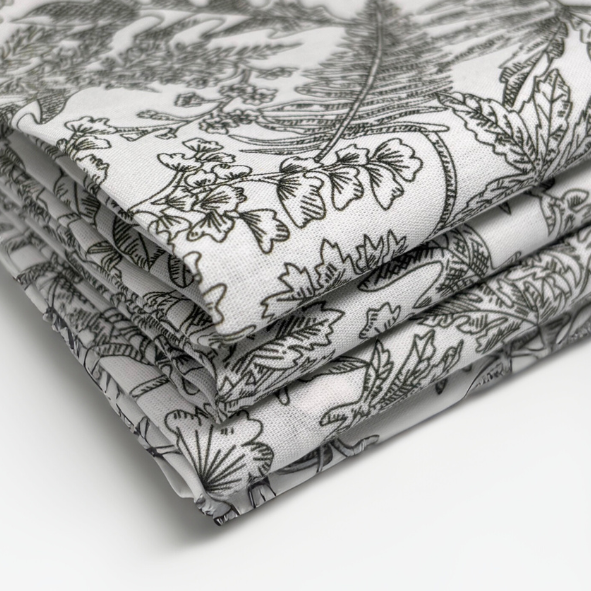 Detailaufnahme eines ordentlich gefalteten Stoffstapels mit filigranem floralen Druck in Dunkelgrün auf naturweißem Untergrund – hochwertiger Naturstoff für zeitlose Wohntextilien im Stil von Fraeulein Matilda.