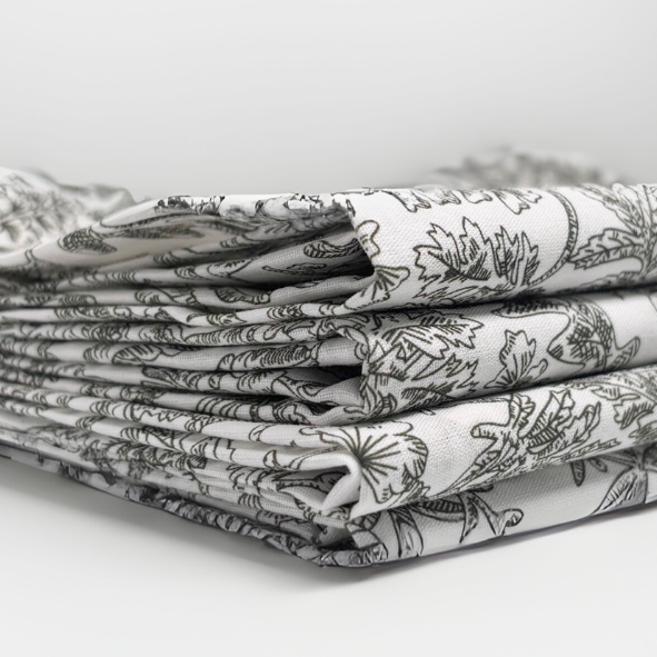 Mehrfach gefalteter Stoffstapel mit detailreichem botanischem Linienmuster in dunklem Grün auf naturweißem Hintergrund – hochwertiger Naturstoff für stilvolle Wohnaccessoires im zeitlosen Design von Fraeulein Matilda.